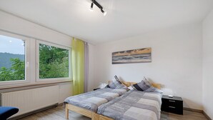 Un dormitorio con cama, mesita de noche, lámpara, ventana con cortinas y un cuadro en la pared.
