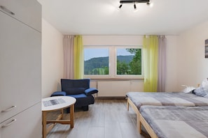 Un dormitorio con cama, una silla, una mesita, un radiador y una ventana con cortinas.