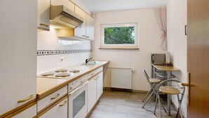 Cocina compacta con estufa, horno y microondas, una ventana con vistas y una pequeña mesa con sillas.