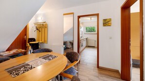 Un comedor con una mesa y sillas, una cocina al fondo, y vistas del exterior por una puerta.