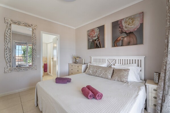 A bedroom with a large bed, a dresser, a mirror, and two paintings on the wall.