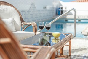 A poolside area with wicker chairs, a glass table with two wine glasses, and a yellow bowl.