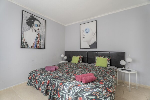 Une chambre à coucher comprenant un lit, des oreillers, une table de chevet et deux œuvres d’art accrochées au mur.