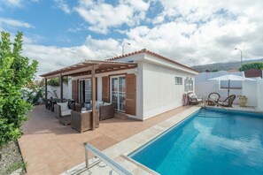 Un espace aménagé au bord de la piscine, comprenant une pergola, du mobilier d’extérieur et une piscine.