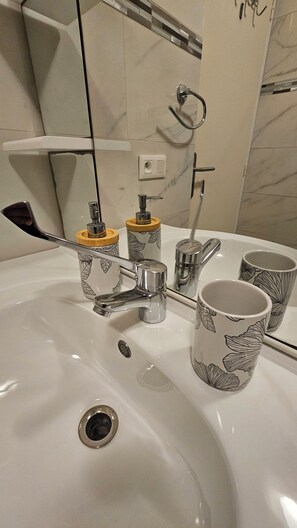 Un lavabo de salle de bain avec un robinet, deux distributeurs de savon et deux tasses décorées.
