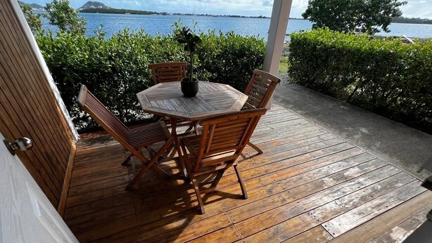 Un terrazzo in legno all'aperto con un tavolo rotondo e sedie, una pianta in vaso e vista sul mare.