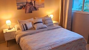 Una camera da letto con un letto, comodini, una ventola a soffitto, un condizionatore d'aria e un quadro raffigurante un tramonto.