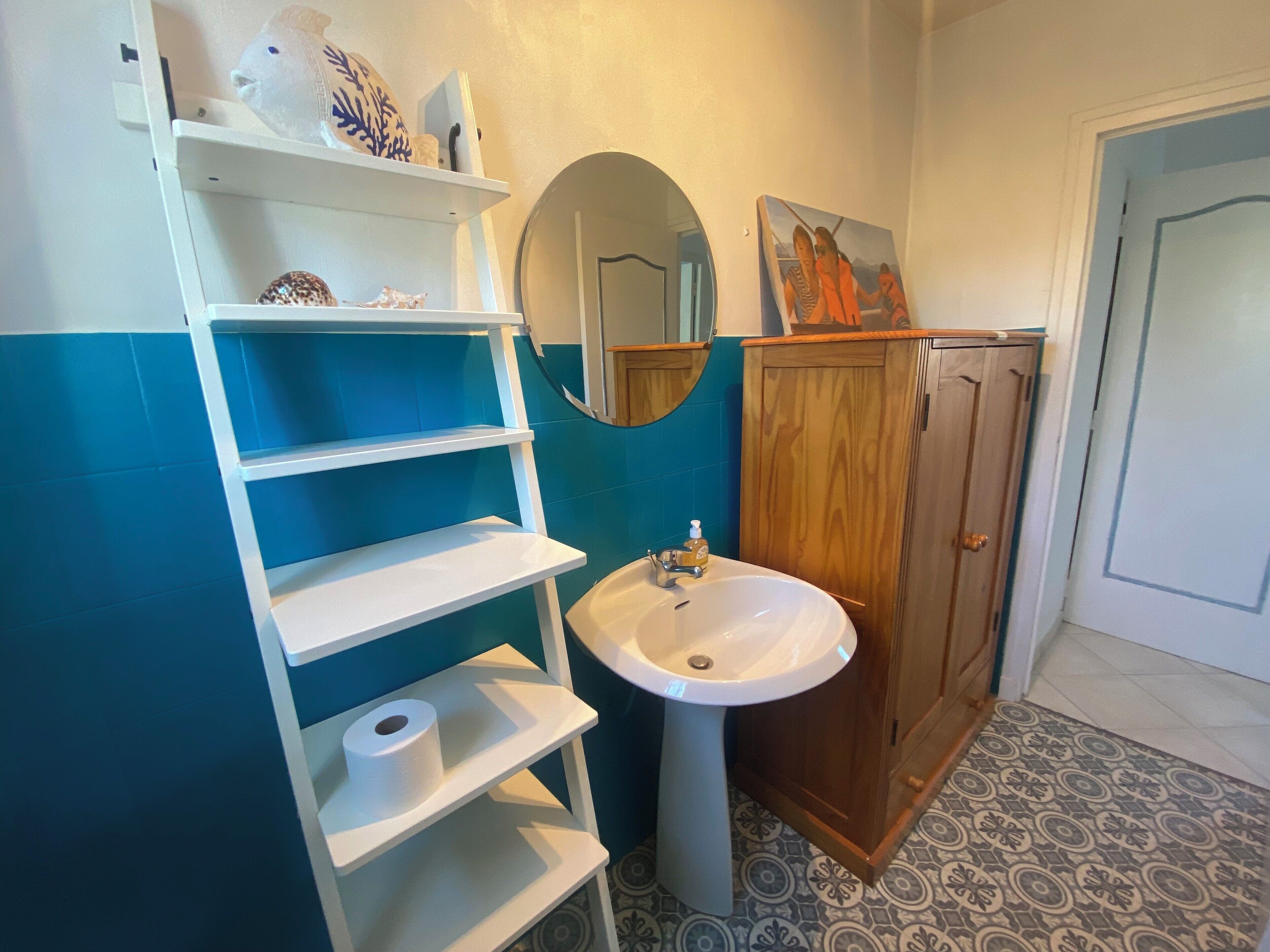 A bathroom with a white sink, a wooden cabinet, a mirror, and a shelf with decorative items.