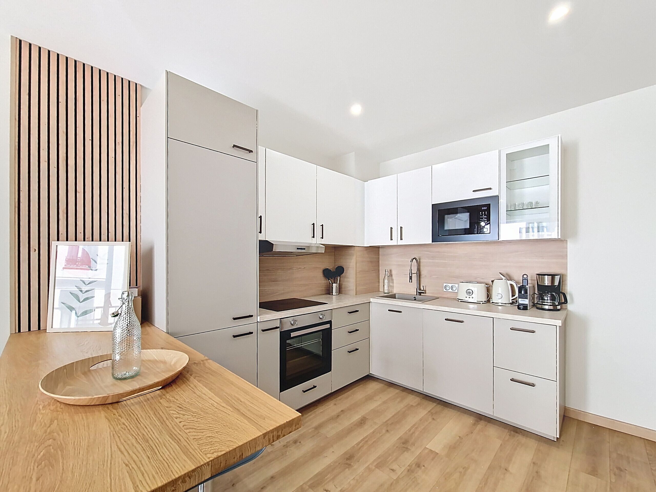 Een moderne keuken met witte kastjes, een houten aanrecht, een magnetron, een koffiezetapparaat en een spoelbak.