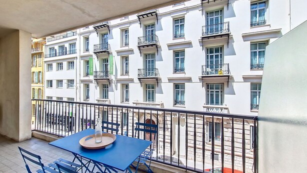 A balcony with a table and chairs, overlooking a row of white buildings with balconies.