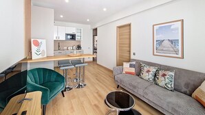 A modern living room with a sofa, a dining area with a table and chairs, a kitchen in the background, and a framed picture on the wall.