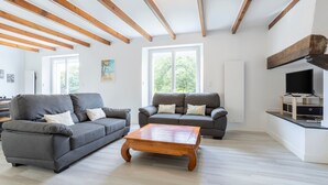 Een moderne woonkamer met twee grijze banken, een houten salontafel en zichtbare houten balken aan het plafond.