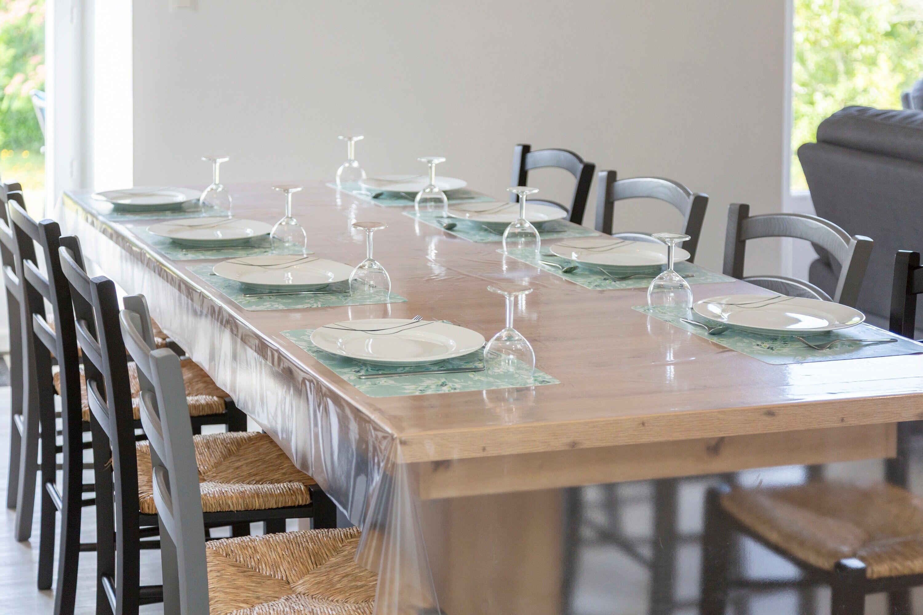 Une longue table à manger, entourée de chaises, mise pour un repas avec des assiettes, des couverts et des verres à vin.