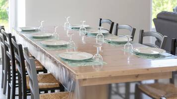 Une longue table à manger, entourée de chaises, mise pour un repas avec des assiettes, des couverts et des verres à vin.