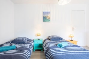 Habitación con dos camas, cada una con ropa de cama a rayas y una mesita de noche color aguamarina con una lámpara.