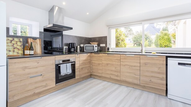 Een moderne keuken met houten kastjes, een ingebouwde oven, een magnetron en een groot raam met uitzicht op groen.