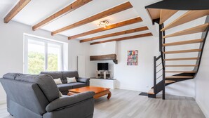 Een moderne woonkamer met een bank, salontafel, houten balken, een open haard en een spiltrap.