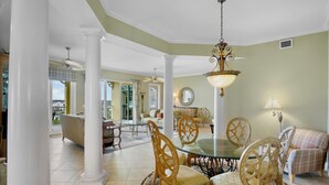 Un comedor amplio con una mesa de vidrio y sillas de madera, rodeado de columnas blancas y una lámpara de araña grande.