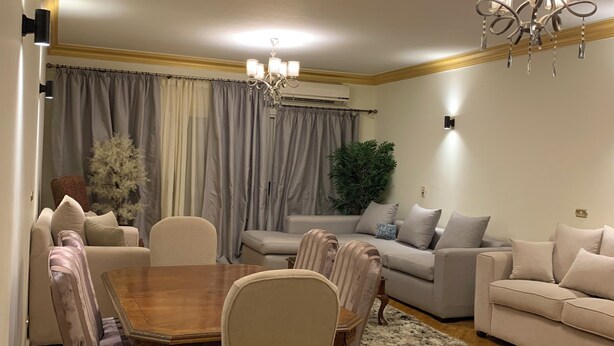 Een moderne woonkamer met een eetgedeelte, met een kroonluchter, banken en een potplant.