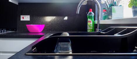Une cuisine moderne avec un plan de travail noir, un saladier rose et un flacon de liquide vaisselle vert.