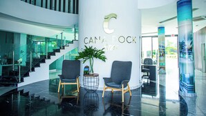 A lobby with a glass staircase, two grey chairs, a potted plant, and a pillar with the logo "CANA ROCK spa". - Cana Rock Star, Cana Bay (Punta Cana)