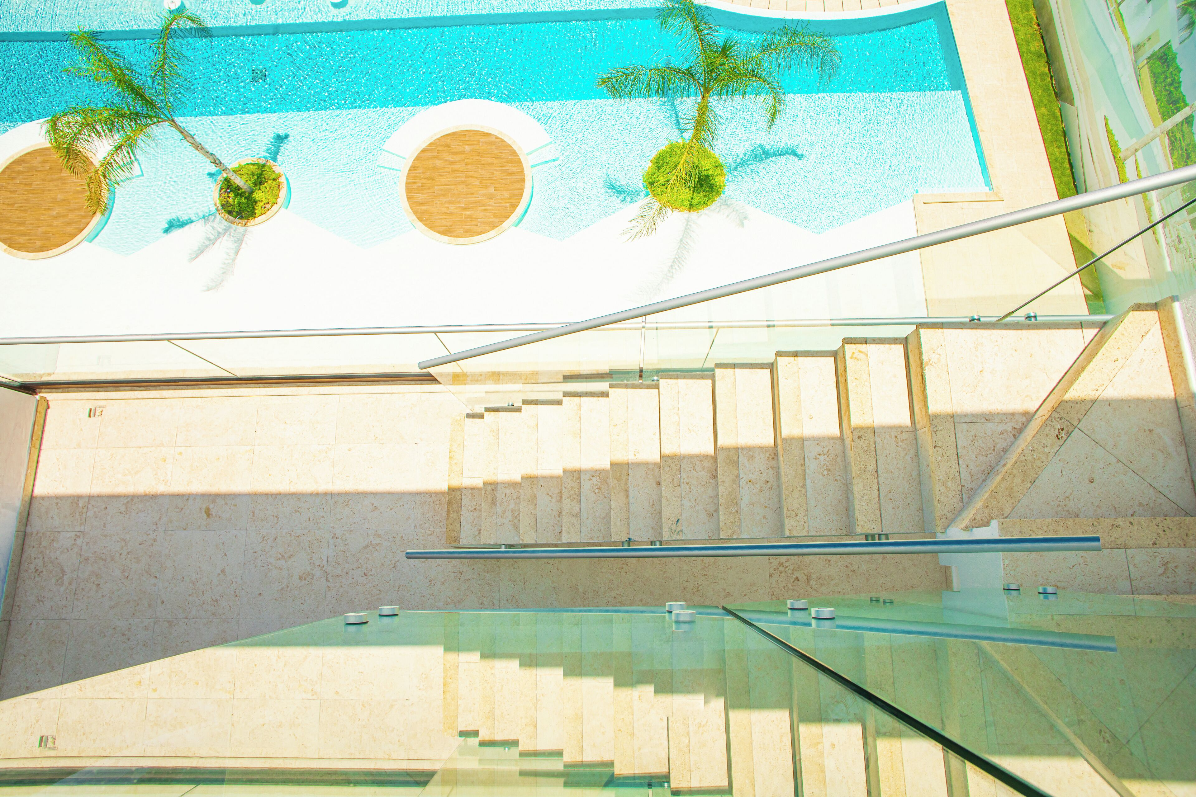 A modern indoor pool area with glass railings and palm trees.