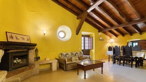 A living room with a fireplace, sofa, coffee table, and dining area with chairs and a table. - Holiday Home 'Amarela' with Mountain View, Shared Pool and Wi-Fi (Meca)