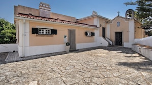 A building with a stone-paved courtyard, a small bell tower, and a door with a cross above it. - Holiday Home 'Amarela' with Mountain View, Shared Pool and Wi-Fi (Meca)