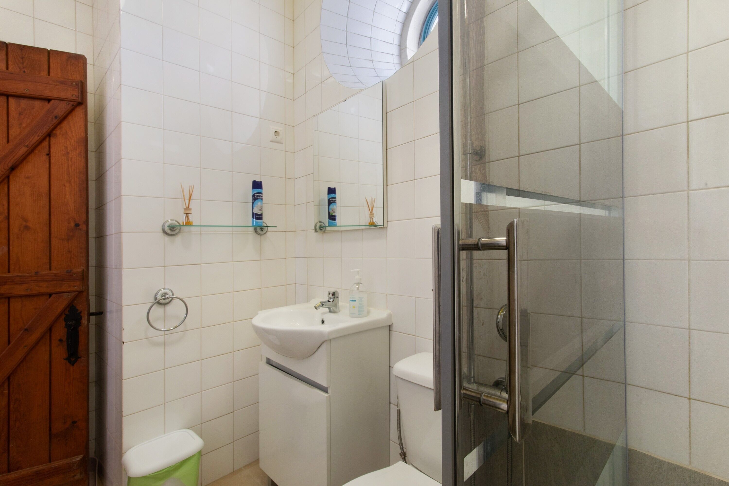 Un baño con puerta de madera, lavamanos, inodoro, cabina de ducha de vidrio y espejo.