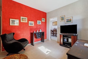 Un salon avec un mur rouge, un canapé noir, un meuble pour la télévision et des tableaux encadrés.