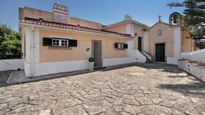 Un edificio con un patio empedrado de piedra, una pequeña torre de campanas y una puerta con una cruz encima.