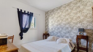 Un dormitorio con cama, mesita de noche, ventana con cortinas y pared con diseño de hojas.