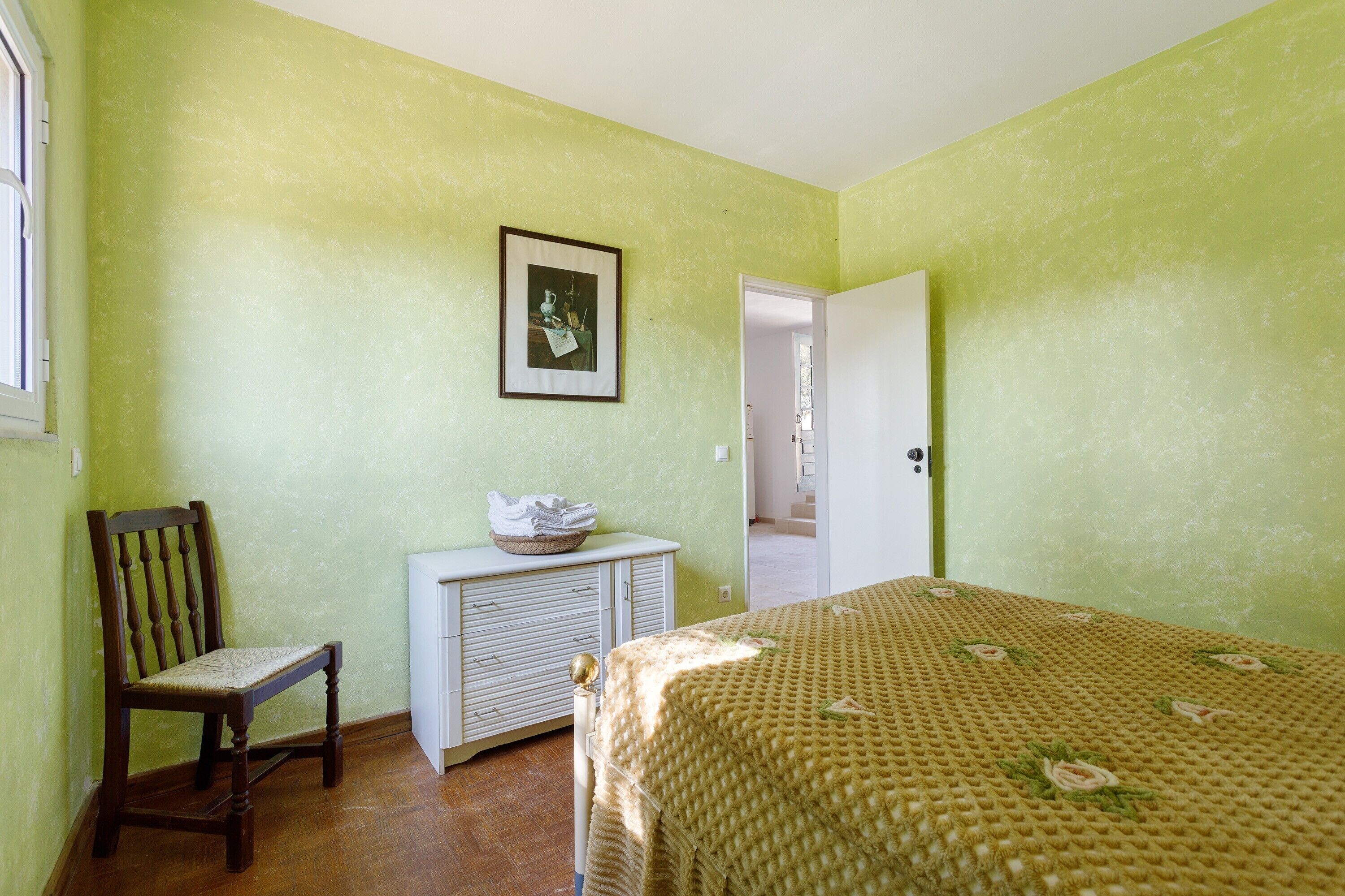 Un dormitorio con cama, una silla, un aparador y una puerta que da a otra habitación.