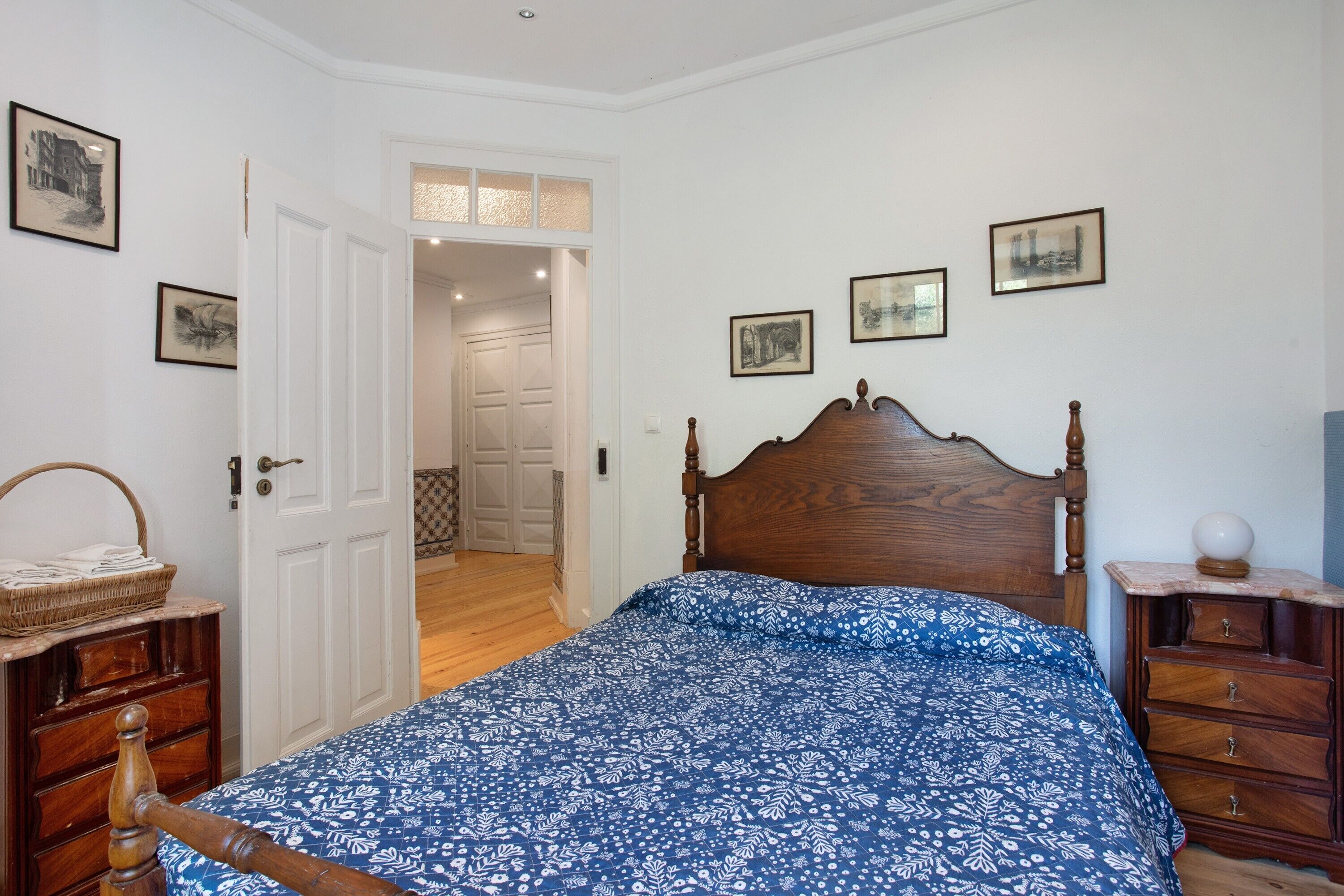 A bedroom with a wooden bed, a dresser, a nightstand, and a door leading to another room.