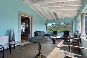 A room with a wooden floor, a round table, several chairs, a sofa, and a view of trees through large windows. - Holiday Home 'Grande' with Mountain View, Shared Pool and Wi-Fi (Meca)