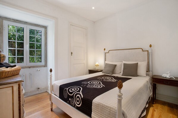 Een netjes opgemaakt slaapkamer met een bed, nachtkastjes, een raam en een dressoir.