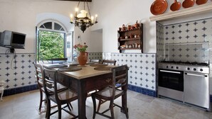 Una cucina con tavolo e sedie, un lampadario, una TV, una finestra e un fornello.