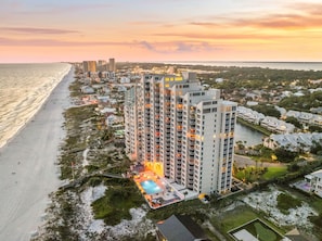 A high-rise hotel with multiple floors, a swimming pool, and a beach view.