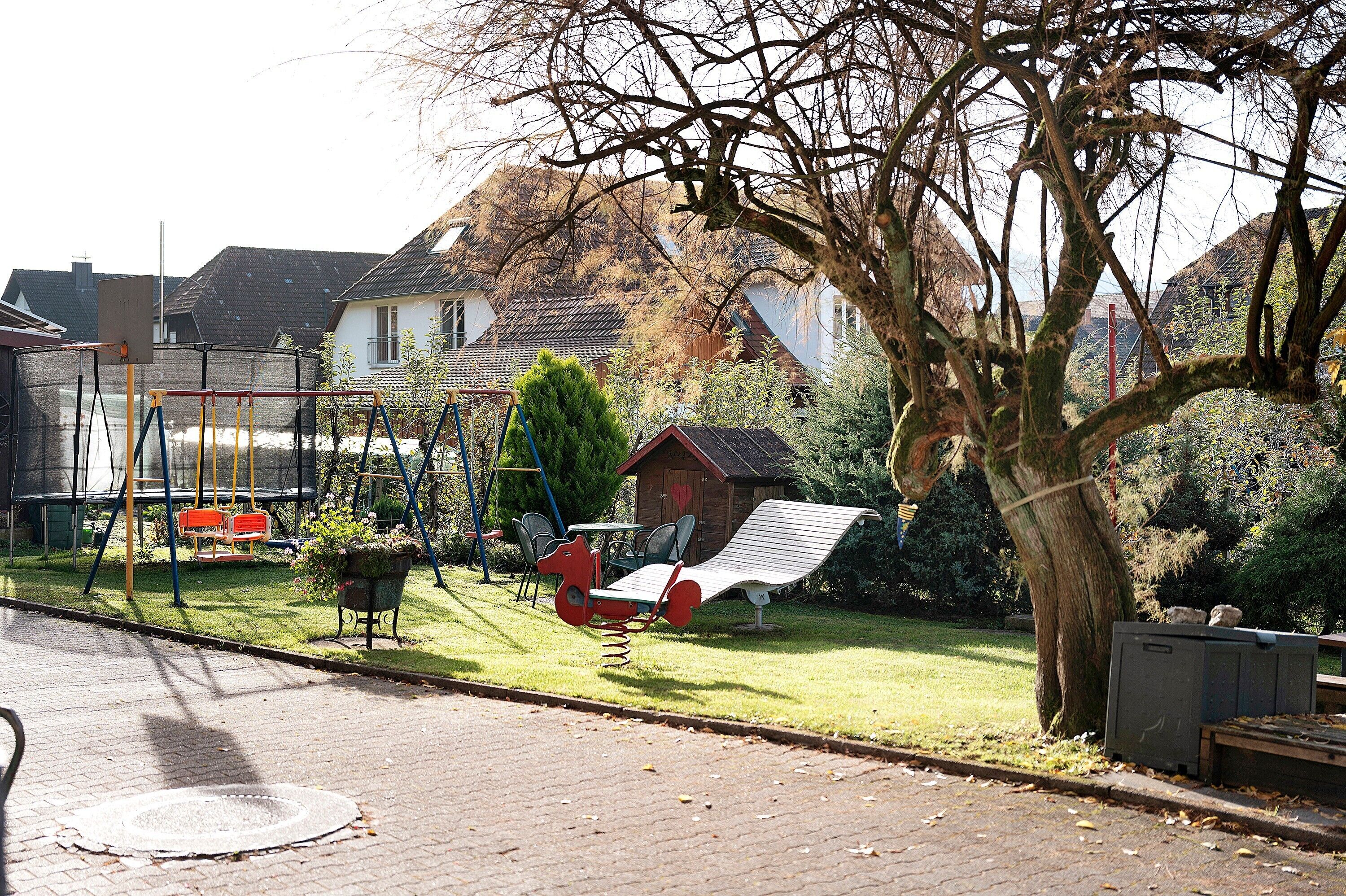 A residential area with a swing set, a red bench, and a small shed.
