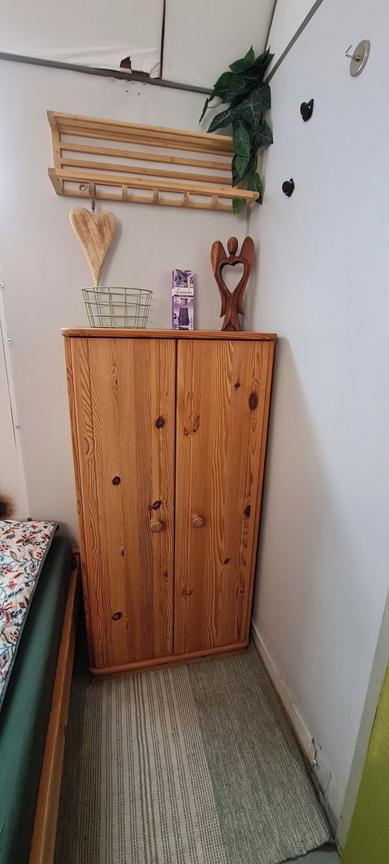 A wooden wardrobe with two doors, a small shelf with a heart-shaped decoration, and a hanging plant.