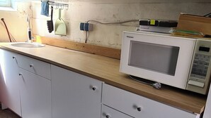 A kitchen with white cabinets, a wooden countertop, a microwave, and a broom leaning against the wall. - Construction trailer on the farm in the Weserbergland (Coppenbrügge)