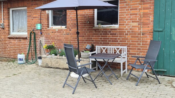 A patio with a table and two chairs, a green umbrella, and potted plants. - Construction trailer on the farm in the Weserbergland (Coppenbrügge)