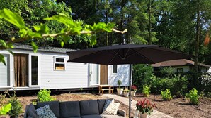 A covered outdoor seating area with a table and chairs, surrounded by greenery and a mobile home in the background. - Nice Holiday Home in Hattemerbroek (Hattemerbroek)