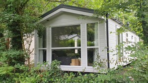 A small, white cabin with large windows, surrounded by dense greenery. - Nice Holiday Home in Hattemerbroek (Hattemerbroek)