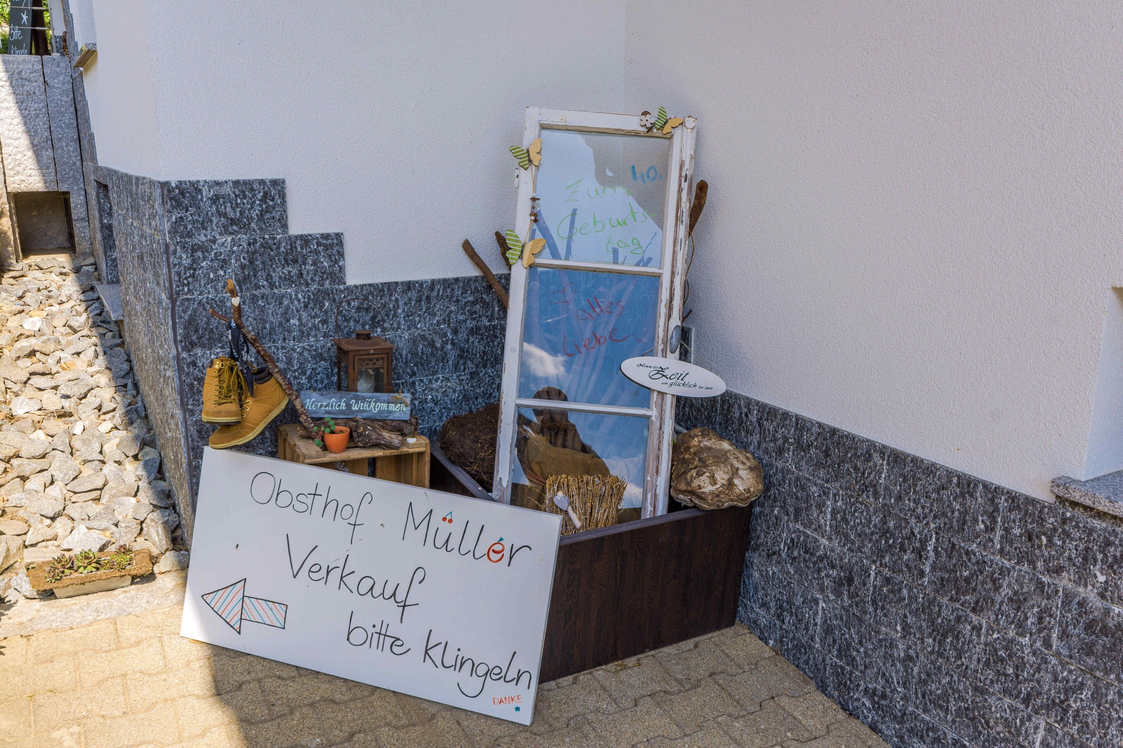 A small outdoor display with a sign, a window with decorations, and a wooden box.