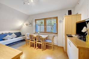 Een ruimtelijk ingerichte leefruimte met een bank, eettafel, stoelen, een televisie en een raam met gordijnen.