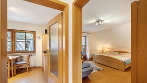 A bedroom with a bed, a window, and a wooden door leading to a dining area with a table and chairs. - Apartment 'Hirschblick' with Mountain View, Shared Terrace and Wi-Fi (Haslach im Kinzigtal)