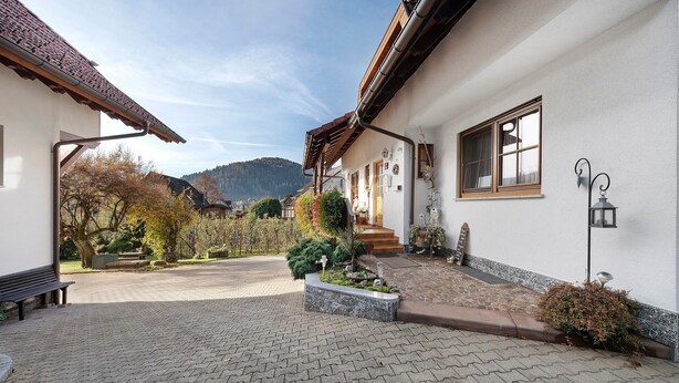 A courtyard with a paved walkway, a bench, a small garden with a cross, and a building with a sloped roof and a window. - Apartment 'Hirschblick' with Mountain View, Shared Terrace and Wi-Fi (Haslach im Kinzigtal)