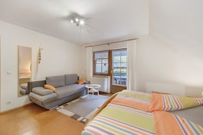 Een kamer met een bank, een bed, een tafeltje en een raam met gordijnen.