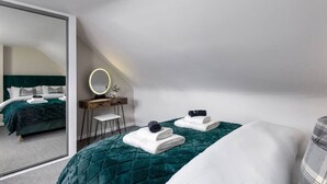 Un dormitorio con un espejo grande, un tocador y dos camas bien hechas.